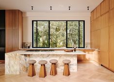 a kitchen with marble counter tops and stools in front of large windows that look out onto the woods