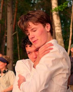 two young men hugging each other in front of trees and people watching them from behind