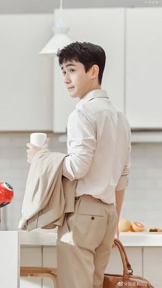 a man holding a coffee cup in his right hand while standing next to a kitchen counter