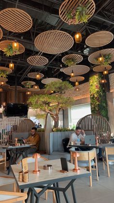 people sitting at tables in a restaurant with plants hanging from the ceiling and round lights above them