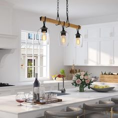 a kitchen island with stools and lights hanging over it, along with wine glasses on the counter