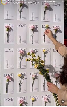 a woman is holding flowers in front of a wall that has love written on it