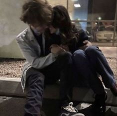 a man and woman sitting on a bench looking at their cell phones in front of a building