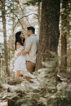 a man and woman standing next to each other in the woods near a tree trunk