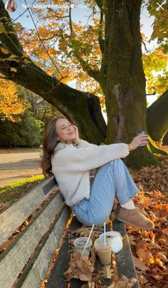 a woman is sitting on a bench in the leaves