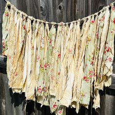 the fabric is hanging on the clothes line by the wooden fence with it's flowered edges