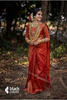 a woman in an orange and gold sari standing on the ground with trees behind her