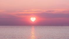 the sun is setting over the ocean with a heart shaped object in the middle of it