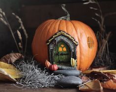 a pumpkin sitting on top of a pile of leaves next to a house shaped like a door