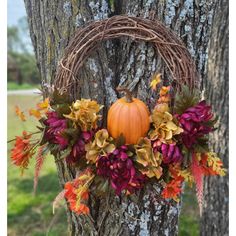 a wreath on the side of a tree decorated with flowers and pumpkins is hanging from it