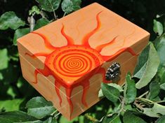 an orange and red box sitting on top of a leaf covered tree branch in front of some green leaves