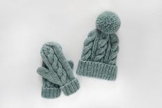 two green knitted mittens and gloves on a white surface