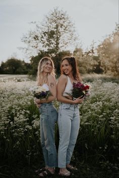 two beautiful young women standing next to each other in front of some tall grass and flowers