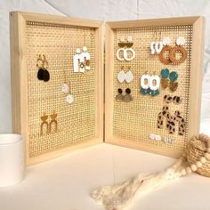 two wooden frames with earrings on them next to a white cup and straw hat holder