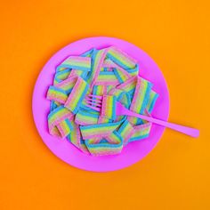 a pink plate topped with lots of rainbow colored candy next to a fork and spoon