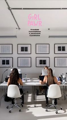 two women sitting at a table with laptops in front of them and pictures on the wall behind them