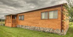 a log cabin sits in the grass under a cloudy sky