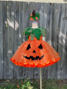 a dress made to look like a pumpkin with leaves on it, sitting in front of a fence