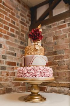 a multi - tiered cake on a gold stand in front of a brick wall