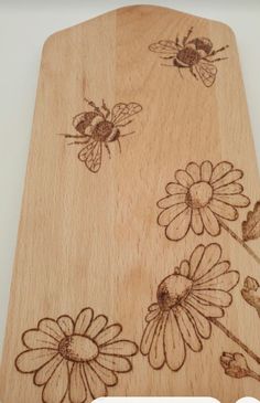 a wooden cutting board with flowers and bees on it