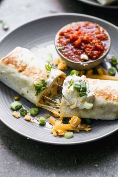 two burritos on a plate with salsa and cheese