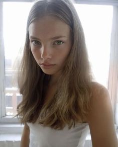 a young woman with long hair standing in front of a window looking at the camera