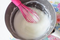 a pink whisk in a metal bowl next to a white cup with milk