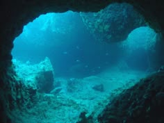 an underwater cave with rocks and fish swimming in the water near it's entrance