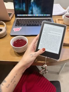 a woman holding an electronic device in front of her laptop