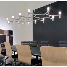 a dining room table with chairs and lights hanging from it's ceiling in front of a black wall