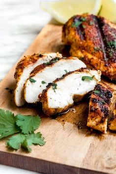 sliced up chicken on a cutting board with parsley and lemon wedges next to it