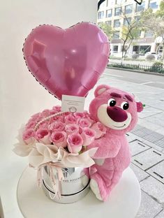 a pink teddy bear sitting on top of a bucket filled with roses and a heart shaped balloon