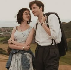 a young man and woman standing next to each other in front of a mountain range