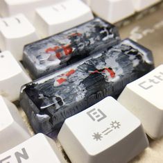 two white keys with black and red designs on them sitting next to each other in front of a computer keyboard