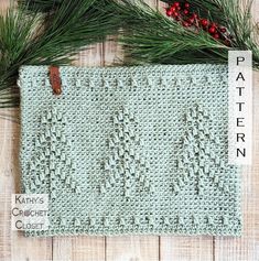 a knitted placemat with pine needles and red berries on the table next to it