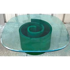 a glass table with a green spiral design on the top, sitting in front of a building