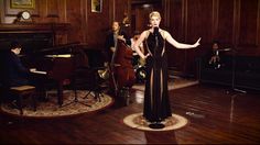 a woman in a black dress standing on top of a wooden floor next to other people