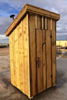 a small wooden outhouse sitting on top of a dirt field next to a blue sky