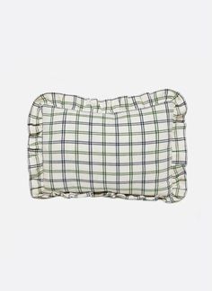 a white and green plaid pillow with ruffles on the edges, sitting against a gray background