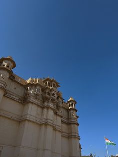 an old building with two flags flying in the air next to it and a blue sky