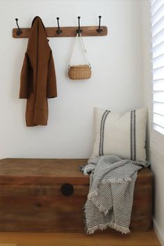 a wooden bench with two coats hanging on it's hooks next to a window