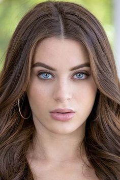 a woman with long brown hair and blue eyes is looking at the camera while wearing large gold hoop earrings