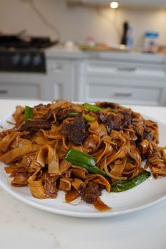 a white plate topped with noodles and meat on top of a table next to green peppers