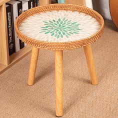 a wooden table with a green flower painted on the top, sitting in front of a bookshelf