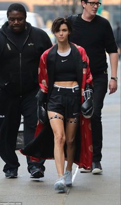 a woman walking down the street with her leg in ripped shorts and black top, while two men walk behind her