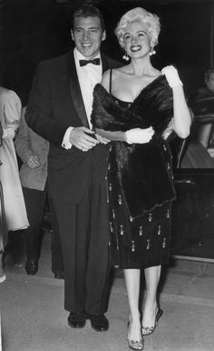 an old black and white photo of a man in a tuxedo standing next to a woman