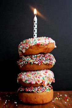 a stack of doughnuts with a lit candle in the middle and sprinkles all around them