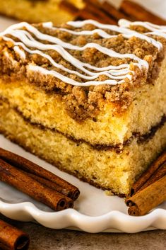 a slice of cinnamon coffee cake on a white plate with cinnamon sticks next to it