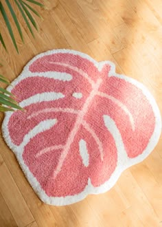 a pink and white rug with a large leaf design on the floor next to a potted plant