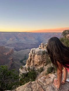 a woman standing on the edge of a cliff looking at the canyon and mountains in the distance